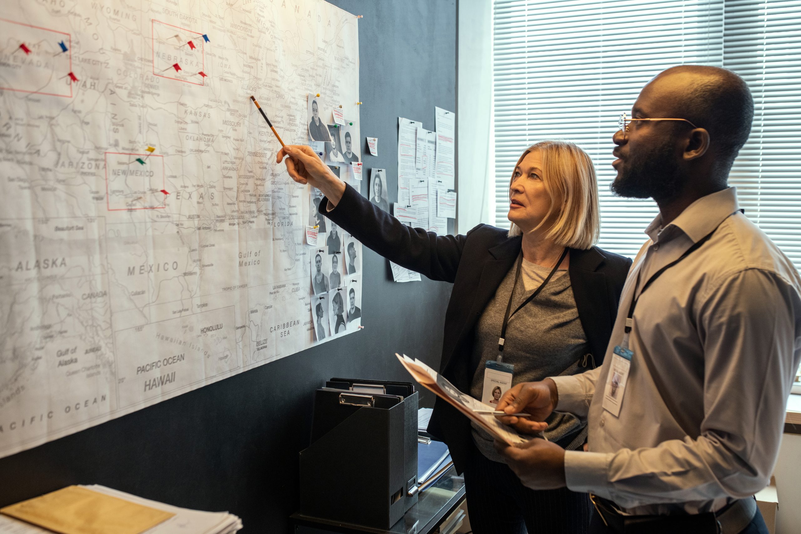 Two FBI agents looking at map on board while mature female pointing at it